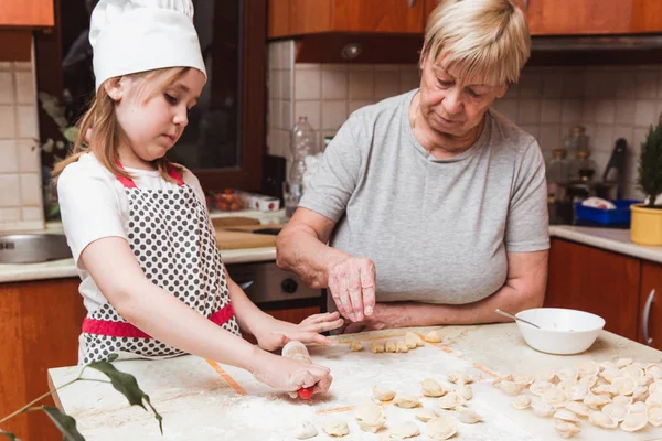 Маленькая девочка с бабушкой на кухне скульпторы пельмени — стоковое фото