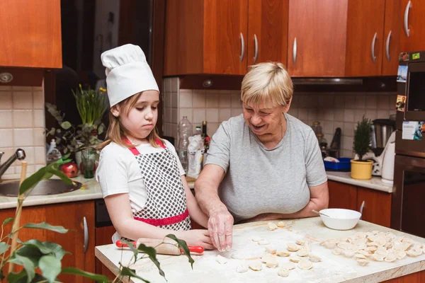 Маленькая девочка с бабушкой на кухне скульпторы пельмени — стоковое фото