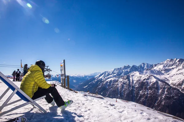 Man zittend op een zonnebank boven op een berg. Hij heeft pauze na het skiën in de besneeuwde Alpen. — Stockfoto