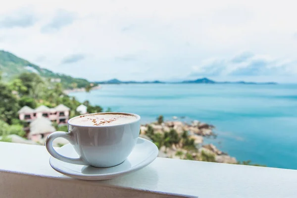 Una taza de café se encuentra en la ventana con una hermosa vista del océano en la isla tropical —  Fotos de Stock