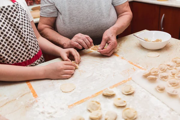Маленькая девочка с бабушкой на кухне скульпторы пельмени — стоковое фото