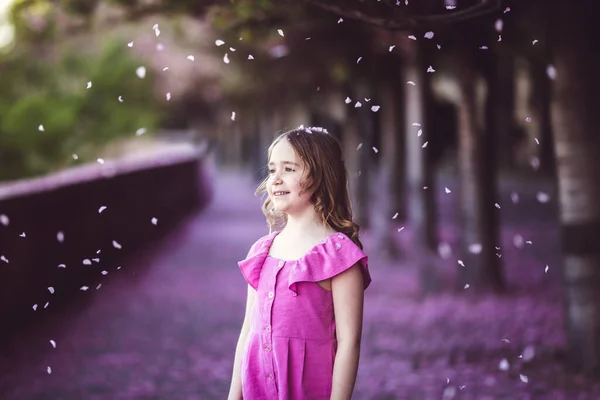 Beautiful girl in pink dress in cherry blossom park on a spring day, flower petals falling from the tree — Φωτογραφία Αρχείου