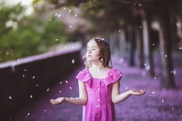 Beautiful girl in pink dress in cherry blossom park on a spring day, flower petals falling from the tree — 스톡 사진