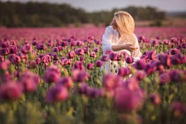 Schöne, glückliche Frau mit langen Haaren im weißen Kleid, die einsam im Flieder-Mohnblumen-Feld spaziert — Stockfoto