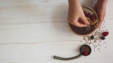 Dişi eller acai smoothie kasesini böğürtlen, yaban mersini, granola ve tohumlarla süslüyor..