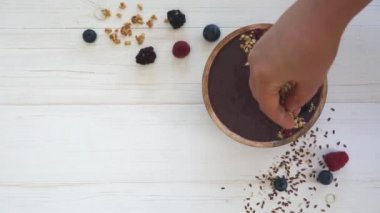 Dişi eller acai smoothie kasesini böğürtlen, yaban mersini, granola ve tohumlarla süslüyor..