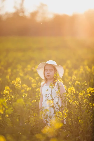 Menina adorável em vestido branco e chapéu no campo de primavera de flores amarelas, estupro — Fotografia de Stock