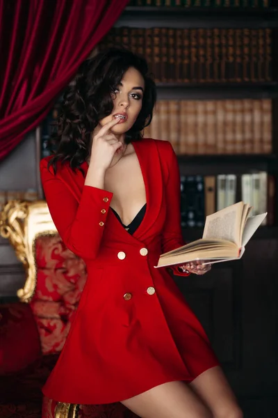 Gorąca dziewczyna w czerwonej sukience dotykając jej usta trzymając książkę w ręce. — Zdjęcie stockowe