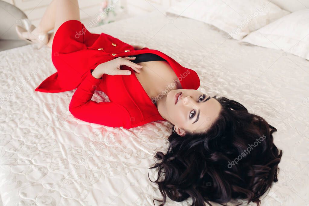 Goergous woman in red dress lying on bed.