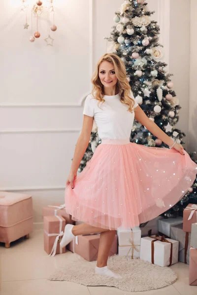 Vacker kvinna i rosa kjol vid julgran. — Stockfoto