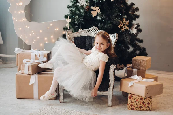 크리스마스 트리 옆 안락 의자에서 편안하게 쉬고 있는 행복 한 어린 소녀. — 스톡 사진