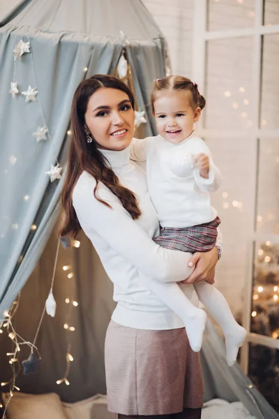 Mother kissing her daughter in cheek. room decorated for Christmas.