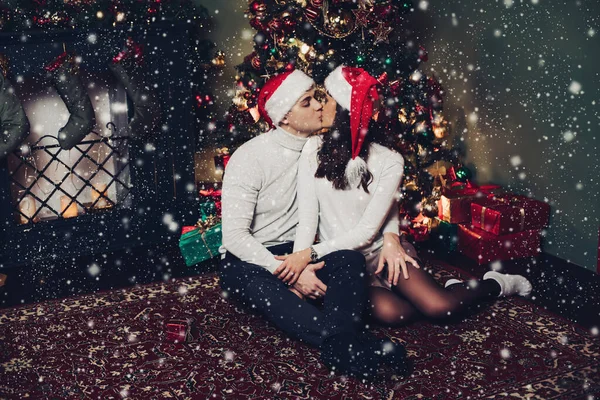 Noel Baba şapkalı çift Noel ağacının yanında öpüşüyor.. — Stok fotoğraf
