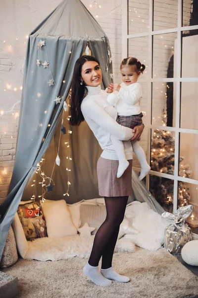 Madre besando a su hija en la mejilla. habitación decorada para Navidad . —  Fotos de Stock