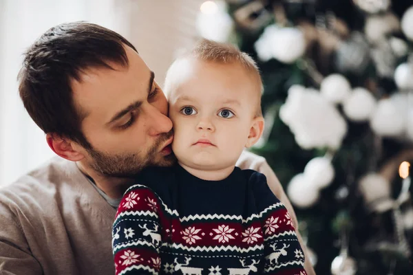 Ο πατέρας φιλάει τον αξιαγάπητο γιο του ενάντια σε ένα ασυγκίνητο χριστουγεννιάτικο δέντρο. — Φωτογραφία Αρχείου