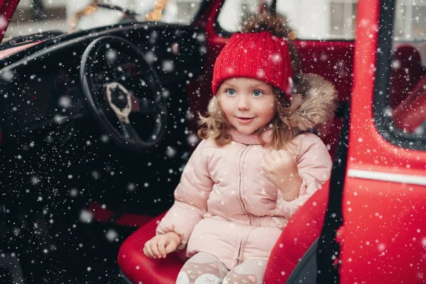 Sonriendo linda chica de invierno en sombrero rojo sentado en el coche divirtiéndose — Foto de Stock