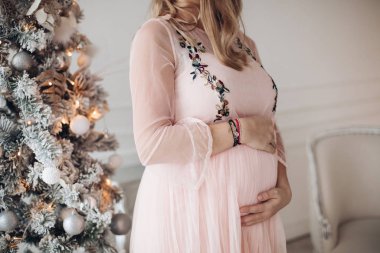 Şefkat dolu bir kadın eli hamile karnına sarılıyor Noel ağacında sevgi hissediyor