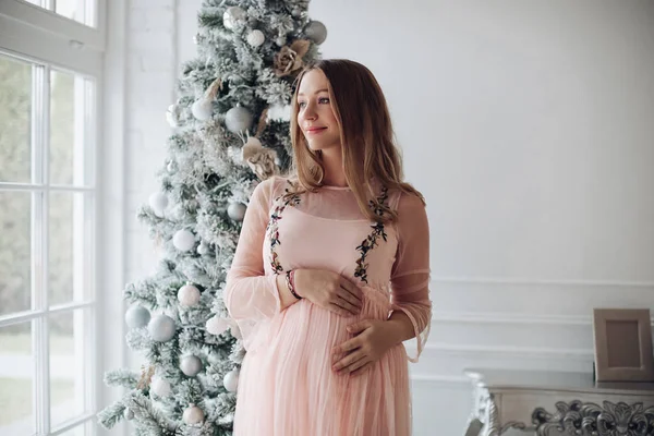 Close-up tenerezza mano femminile abbracciare pancia incinta sensazione di affetto all'albero di Natale — Foto Stock