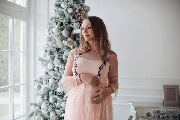 Şefkat dolu bir kadın eli hamile karnına sarılıyor Noel ağacında sevgi hissediyor