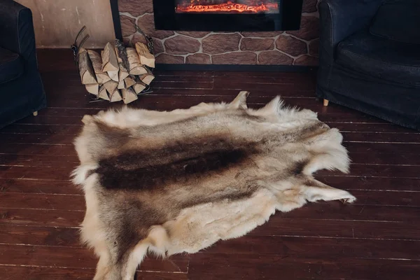 Fur skin on the wooden floor. View over genuine fox fur skin next to pile of wooden logs on the brown wooden floor.