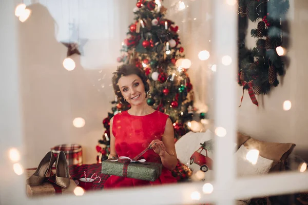 Ganska leende kvinna sitter i sitt sovrum med julklapp — Stockfoto