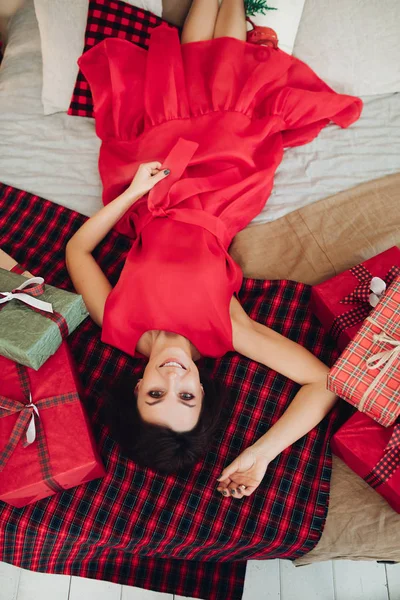 Gülümseyen çekici bayan hediyelerin yanında, ekose üzerinde yatıyor. — Stok fotoğraf