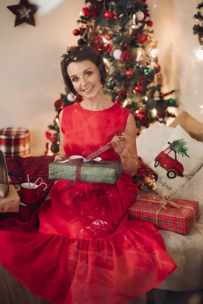 Güzel, gülümseyen bir kadın Noel hediyesiyle yatak odasında oturuyor. — Stok fotoğraf