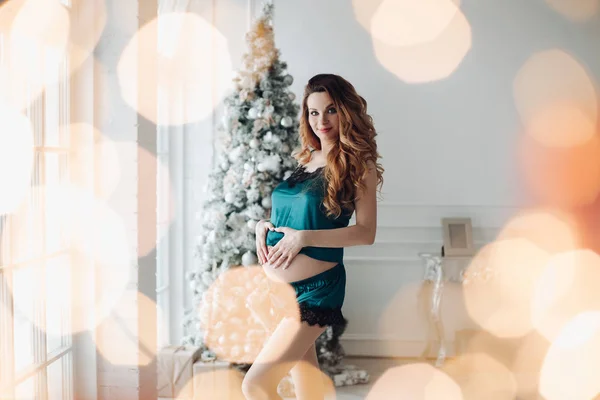 Hermosa moda embarazo chica joven en pijama posando en el fondo del árbol de Navidad — Foto de Stock