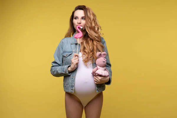 Amuzant casual gravida fata pozand cu iepure jucărie dulce bomboane izolate la galben studio fundal — Fotografie, imagine de stoc