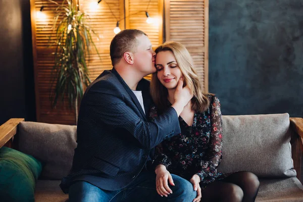 Retrato de casal romântico sentado no sofá cinza em estúdio decorado . — Fotografia de Stock