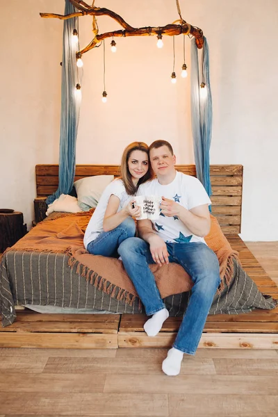 Ρομαντικό ζευγάρι κάθεται στο κρεβάτι, με δημιουργικό κύπελλο στο χέρι. — Φωτογραφία Αρχείου