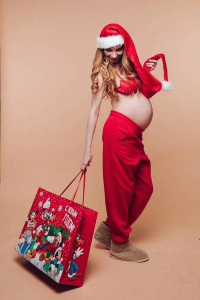 11 27 2019 Belarus Minsk: Crăciun fericit fată gravidă în costum de Moș Crăciun care deține cadou de vacanță având emoții pozitive — Fotografie, imagine de stoc