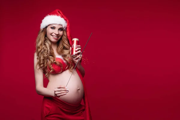 11 27 2019 Belarus Minsk: O tânără însărcinată adorabilă în costum de Moș Crăciun care prezintă o burtă mare izolată la studioul roșu — Fotografie, imagine de stoc