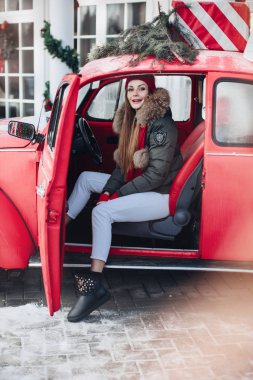 Belarus Minsk 16: 12: 2019: Hoş, modaya uygun, kış kızı, kar taneleriyle çevrili kırmızı klasik arabaya poz veriyor.