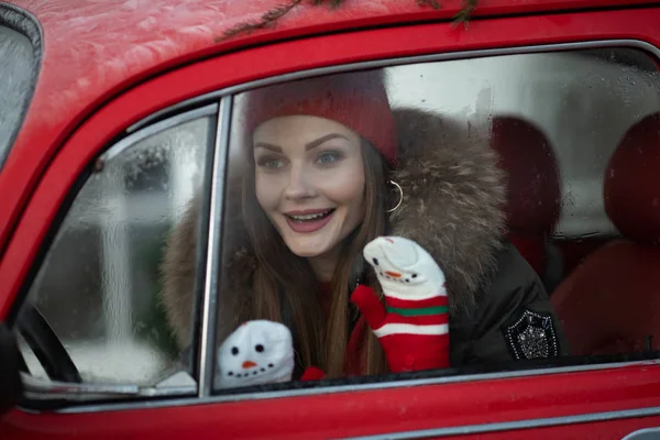 Belarus Minsk 16 12 2019:Pleasant fashionable winter girl smiling posing at red vintage car surrounded by snowflakes — 스톡 사진