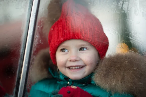 Χαμογελώντας χαριτωμένο κορίτσι του χειμώνα σε κόκκινο καπέλο κάθεται στο αυτοκίνητο διασκεδάζοντας — Φωτογραφία Αρχείου