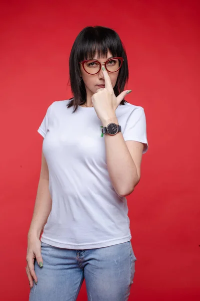 Mujer casual enfocada tocando gafas en la cara posando en el fondo rojo del estudio —  Fotos de Stock