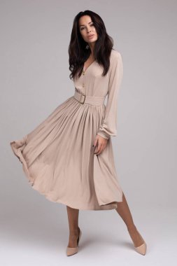 Zarif, genç, gülümseyen esmer kız beyaz arka planda izole edilmiş şık bir elbise içinde poz veriyor.