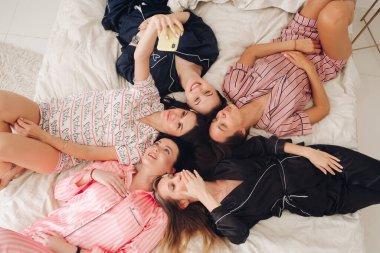 Pretty girls in pyjamas taking selfie on bed. clipart