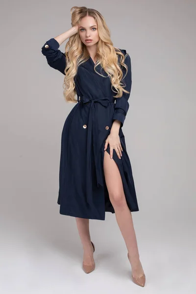 Pretty young lady in elegant trench coat walking in studio — 스톡 사진