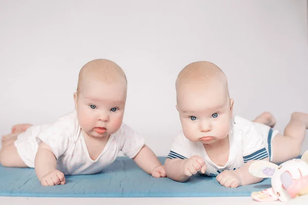 Two beautiful little babies lies on a bed together and looks to the camera — Stock Photo, Image