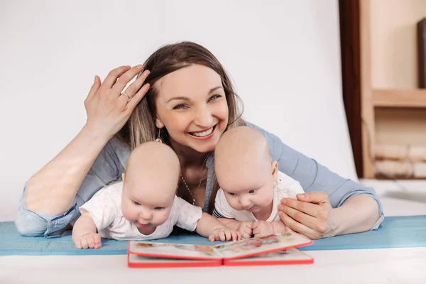 Mooie jonge moeder met haar kinderen glimlacht en lees een boek — Stockfoto