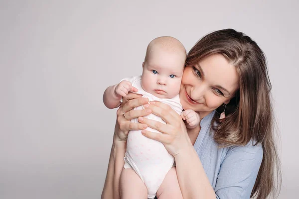 Hermosa joven madre sostiene al niño en sus manos y se ve feliz — Foto de Stock