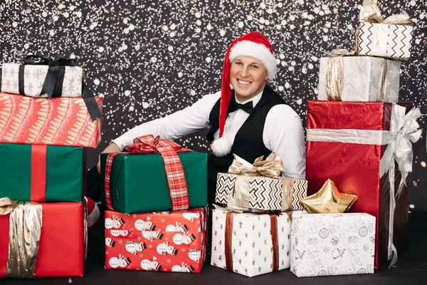 Hombre sonriente en traje con sombrero de Papá Noel posando con regalo de Navidad rodeado de nieve —  Fotos de Stock