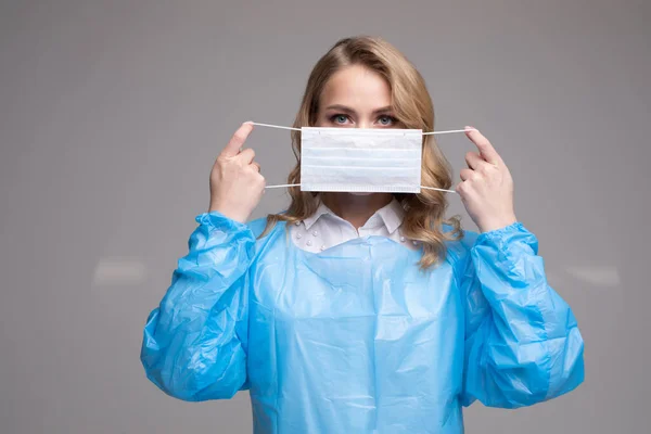 Portrait of woman in protective uniform putting on safety medical mask on face