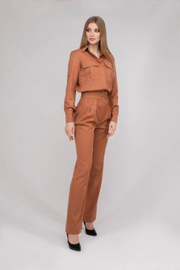 Attractive young blonde model with perfect slim body posing in trendy orange pantsuit full length