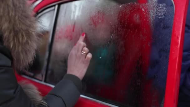 Primer plano femenino dibujo a mano forma de corazón en hielo coche ventana 4k metraje — Vídeo de stock