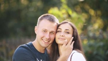 Gülümseyen bir çift yaz parkında birbirlerine sarılıp öpüşüyorlar.