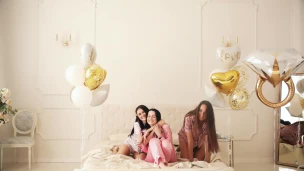 Три девушки сидят на кровати и радуются вместе на пижамной вечеринке — стоковое видео