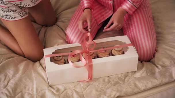 Mädchen sitzt auf einem Bett mit Geschenken und öffnet die Schachtel mit leckeren Cupcakes